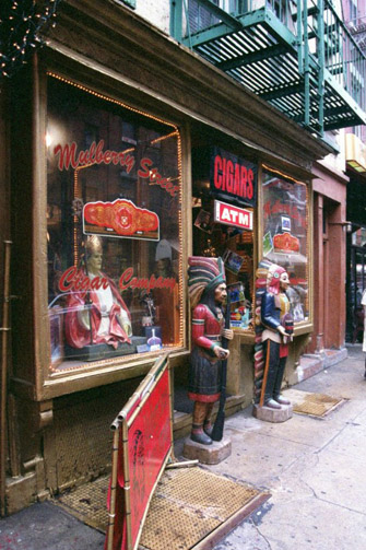 Figura 7. Una estatua de San Gennaro, el patrón de Nápoles. En su figura se basta la mayor fiesta del barrio, la que atrae a decenas de miles de visitantes. En la imagen, la imagen del santo descansa en la vitrina de una tienda de cigarros cuya puerta está resguardada por dos estatuas indias de madera.